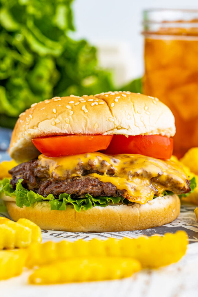 smash burger with lettuce and tomato in front of a glass of iced tea