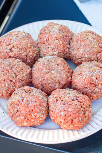 ground beef portioned and rolled into balls for smash burger, top with seasoning on a plate