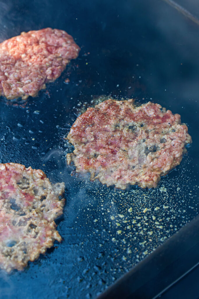 smashed ground beef ball topped with seasoning on a hot griddle