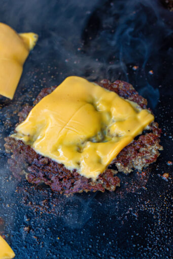 smash burger topped with american cheese on a hot griddle