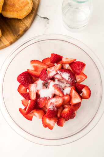 quartered strawberries, water, and sugar in a glass mixing bowl