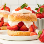 square image of biscuit strawberry shortcakes on small plates next to fresh strawberries