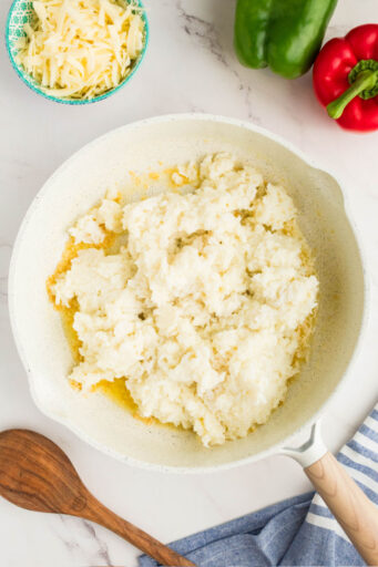 pureed cauliflower mixed with cooked rice in a skillet with melted butter and garlic