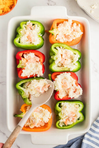 shrimp and cheesy rice mixture being spooned into cleaned bell pepper halves in a baking dish