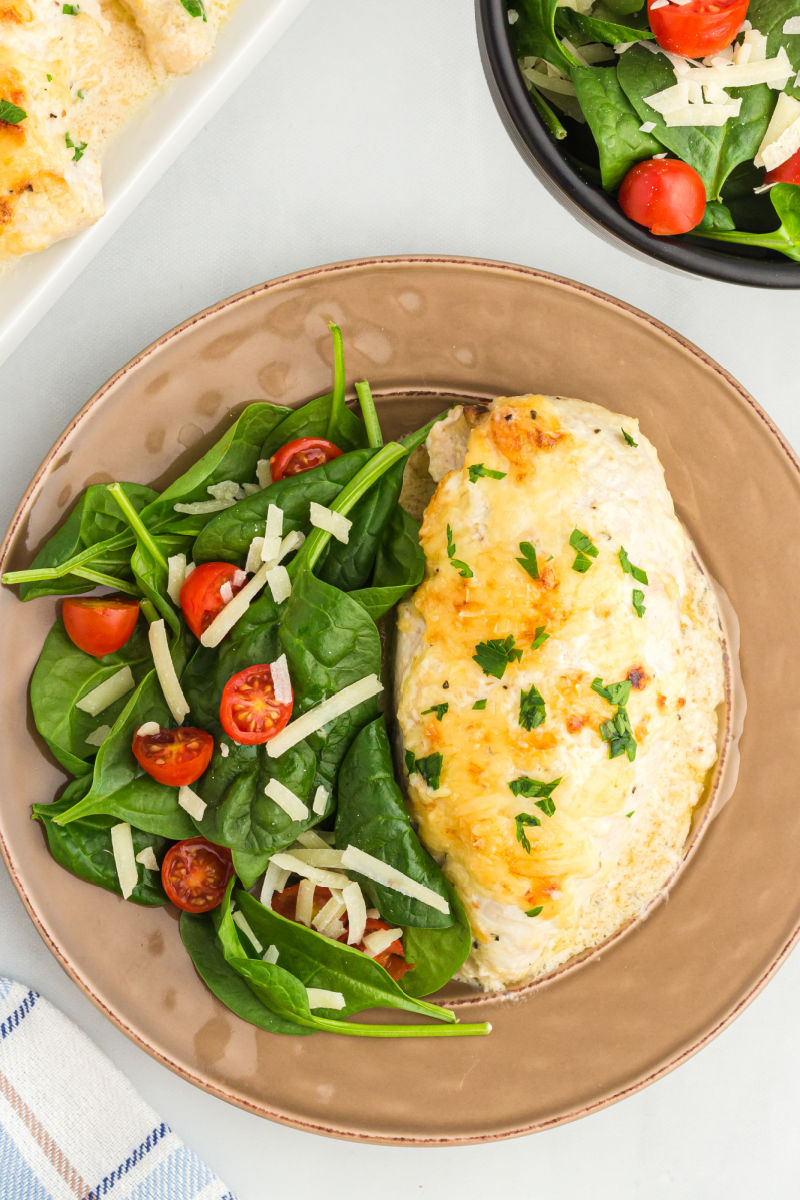 baked caesar chicken on a dinner plate with a green salad