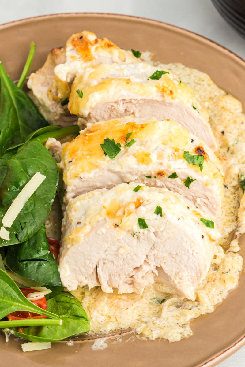 baked caesar chicken cut into slices on a plate with a salad