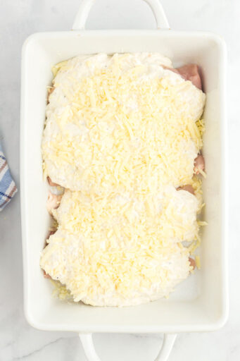 caesar dressing mixture spread over chicken breasts in a baking dish and topped with shredded parmesan