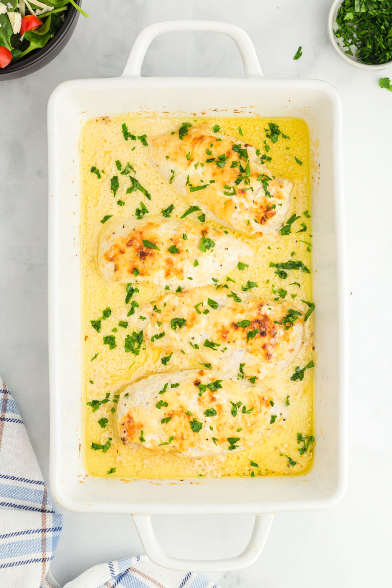 baked caesar chicken with chopped parsley on top in a ceramic baking dish