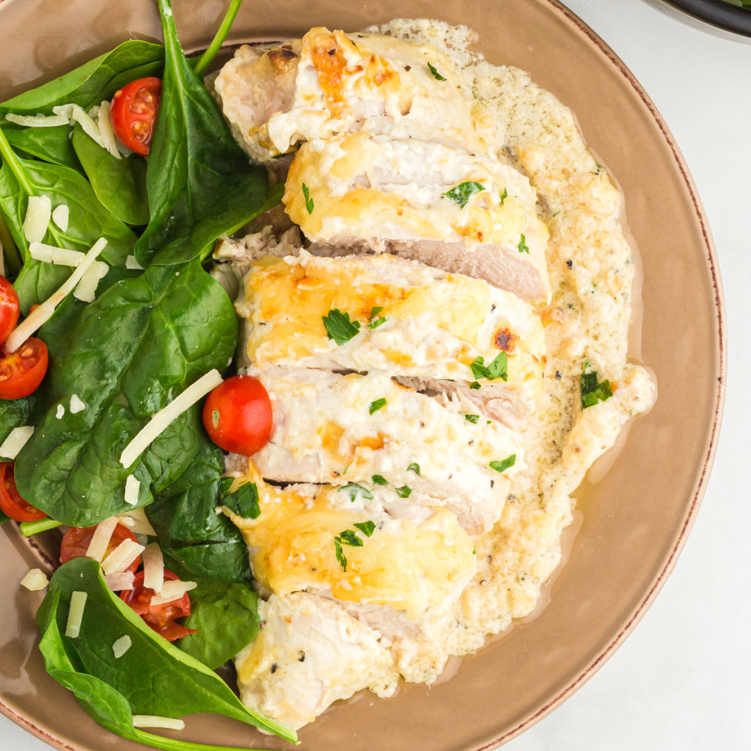 square image of baked caesar chicken cut into slices on a dinner plate with a green salad