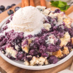 square image of blueberry cobbler topped with vanilla ice cream on a plate