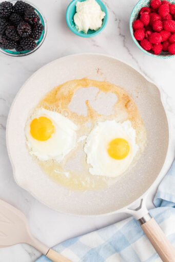 two eggs partially cooked eggs in a skillet with melted butter