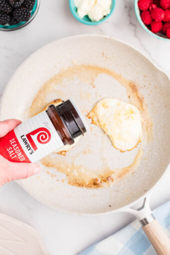 lawry's seasoned salt being sprinkled over two fried eggs in a skillet