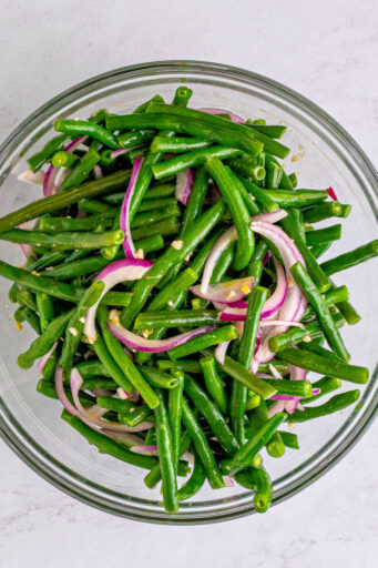 green beans and sliced red onions tossed in vinaigrette in a glass bowl