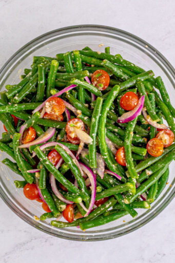 marinated green bean salad tossed with grated parmesan and halved cherry tomatoes in a glass bowl