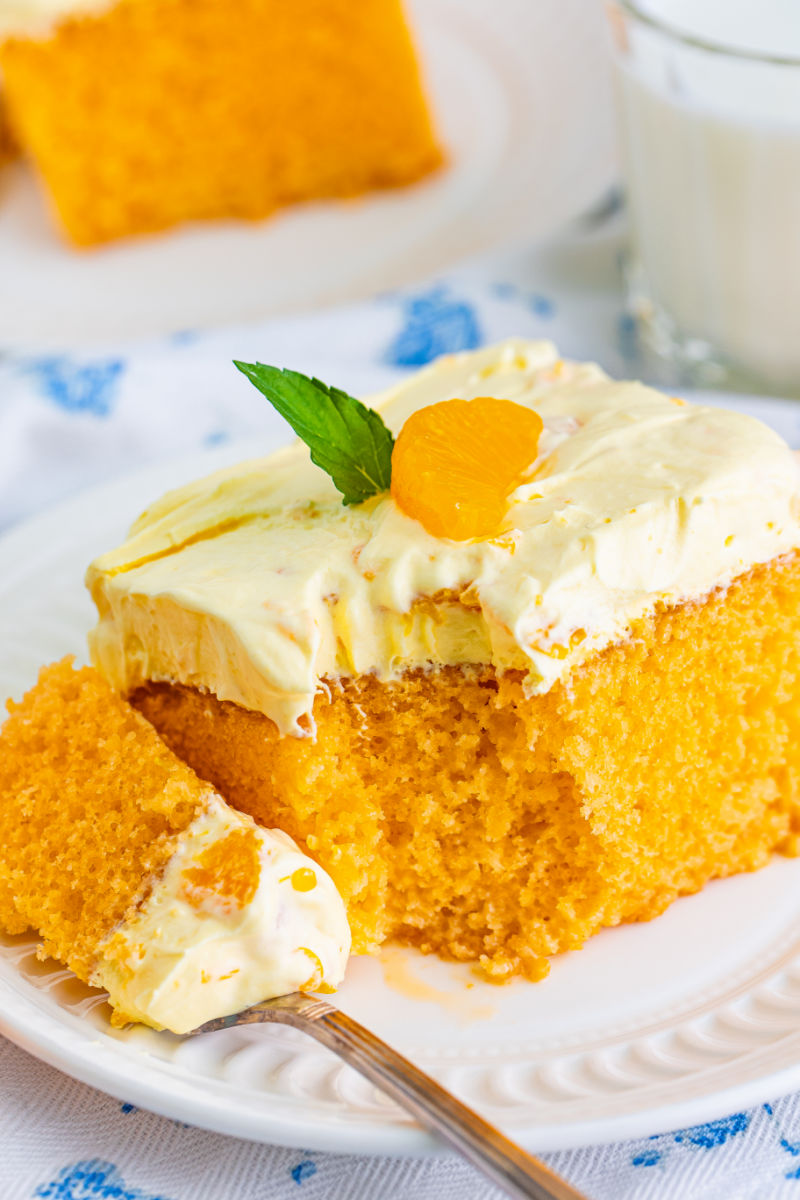 bite of orange creamsicle cake on a fork resting next to the slice on a white plate