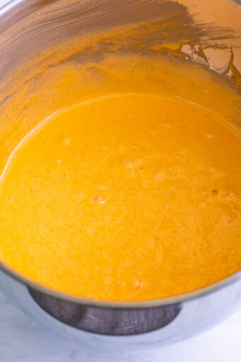 white cake batter mixed with orange gelatin in a mixing bowl