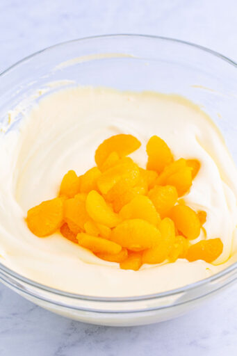 mandarin orange segments added to a bowl of vanilla mousse