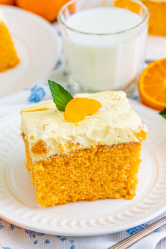 slice of orange creamsicle cake on a plate with a mandarin orange segment and mint left on top for garnish
