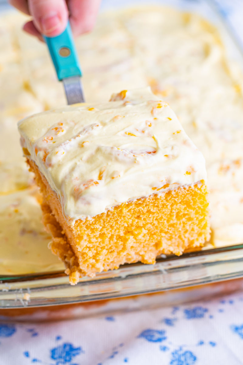 slice of orange creamsicle cake on a spatula over the baking dish