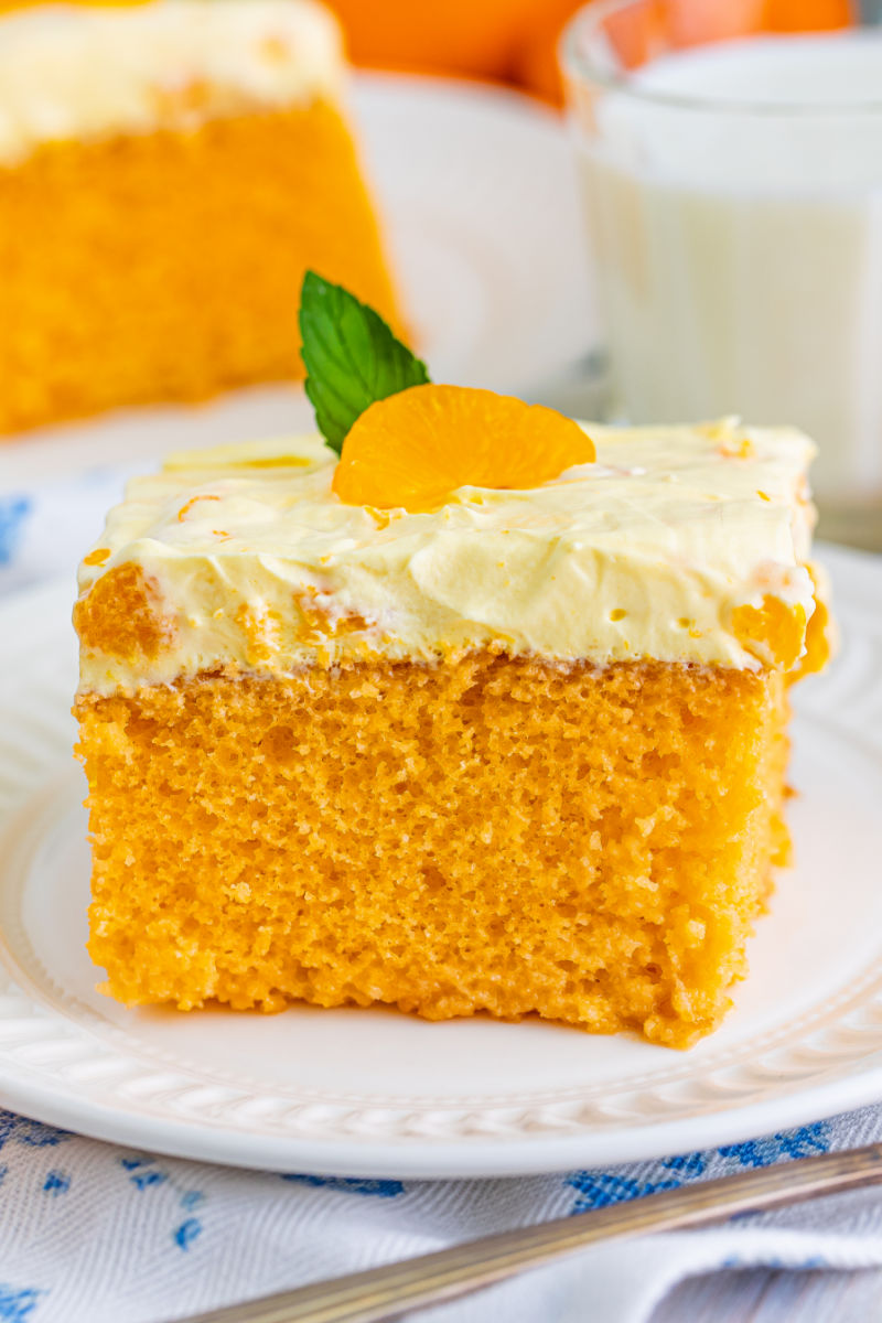 slice of orange poke cake on a small white plate next to a glass of milk