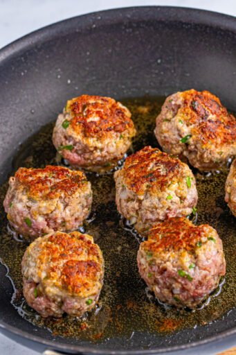 italian meatballs being seared in a skillet with olive oil