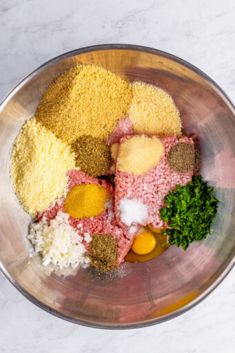 ground pork, beef, and veal in a large mixing bowl with cheeses, bread crumbs, seasonings, eggs, onion, and parsley