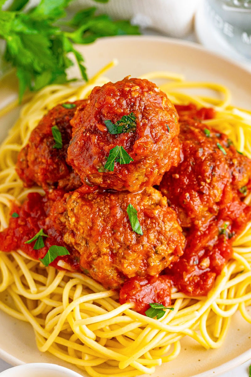 angled view of homemade italian meatballs and sauce served over a plate of spaghetti