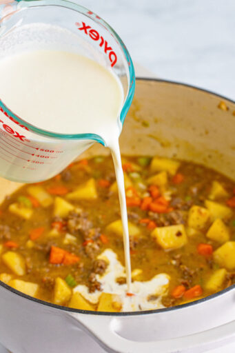 half and half being poured into a pot with veggies, ground beef, and beef broth