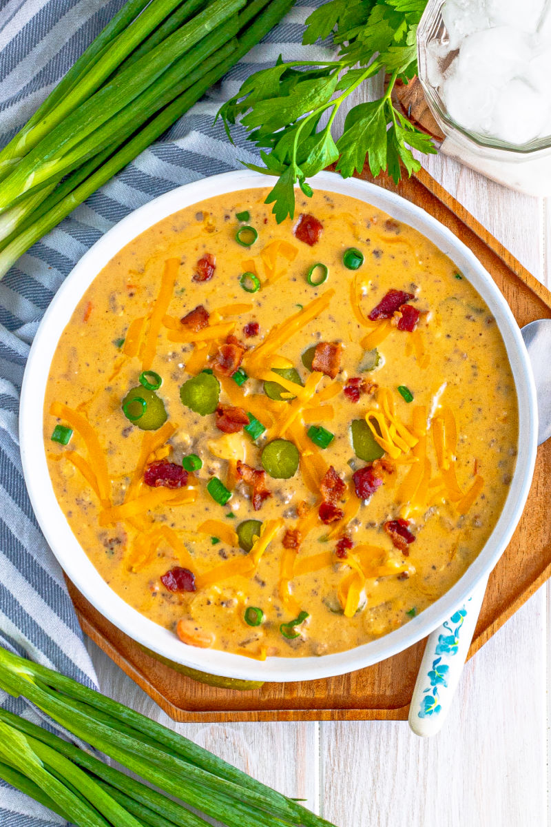 looking down at a bowl of bacon cheeseburger soup next to a spoon on a wooden serving tray