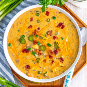 square image of bacon cheeseburger soup topped with cheese, bacon, green onions, and pickle