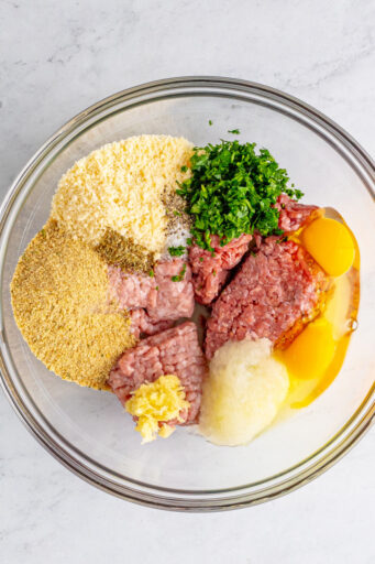 ground beef, pork, grated onion, breadcrumbs, eggs, parmesan, and seasonings in a glass mixing bowl