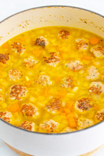 browned meatballs and uncooked orzo added to italian wedding soup base in a large pot