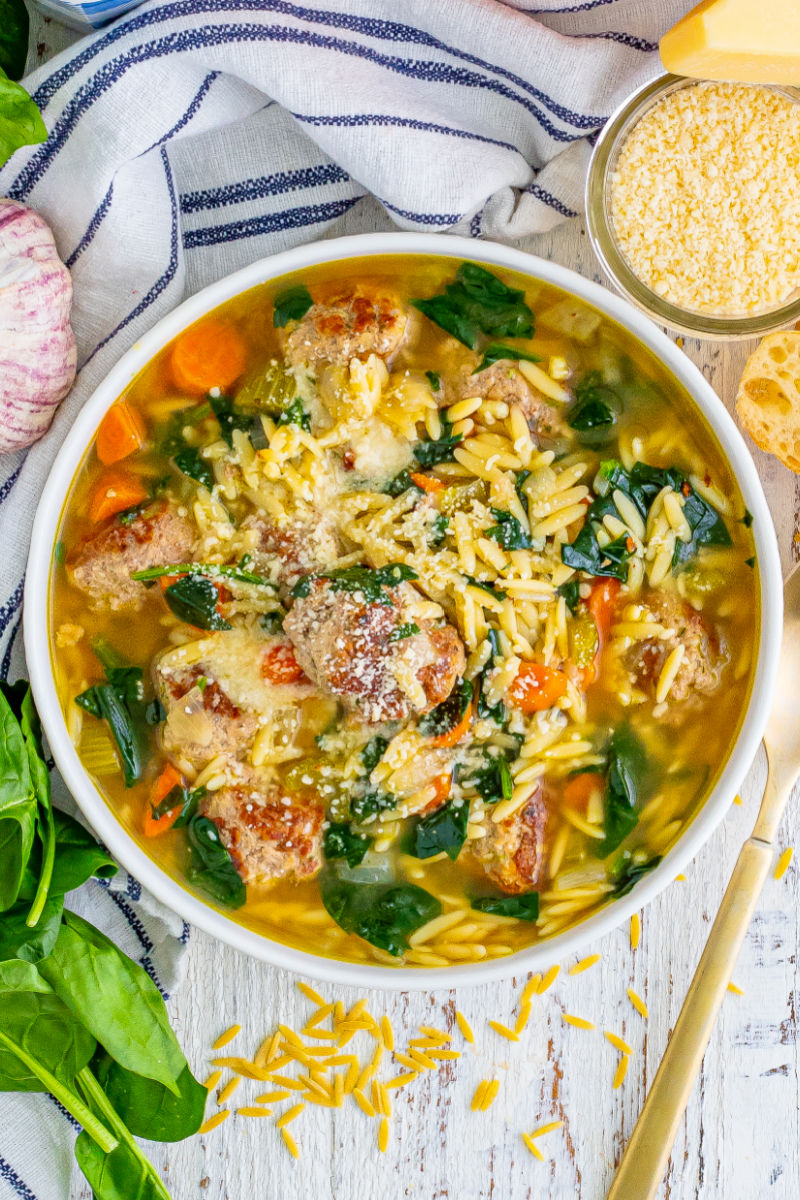 looking down at a bowl of homemade wedding soup next to a spoon and a bowl of grated parmesan