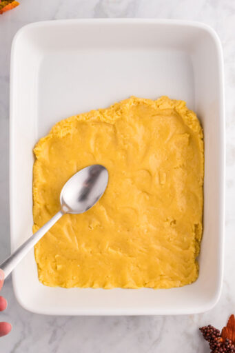 yellow cake mix crust being pressed into a 9x13 baking dish