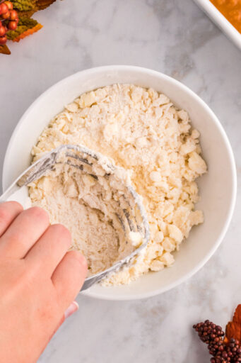 hand using a pastry cutter to cut cold butter into cake mix in a bowl