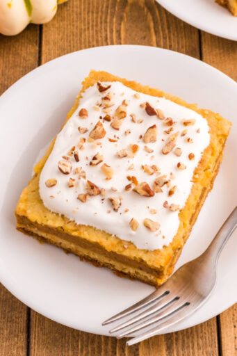 slice of pumpkin pie cake topped with whipped cream and pecans on a plate with a fork