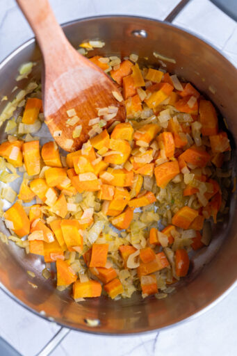 sautéed carrots and onions in a large pot with a wooden spoon