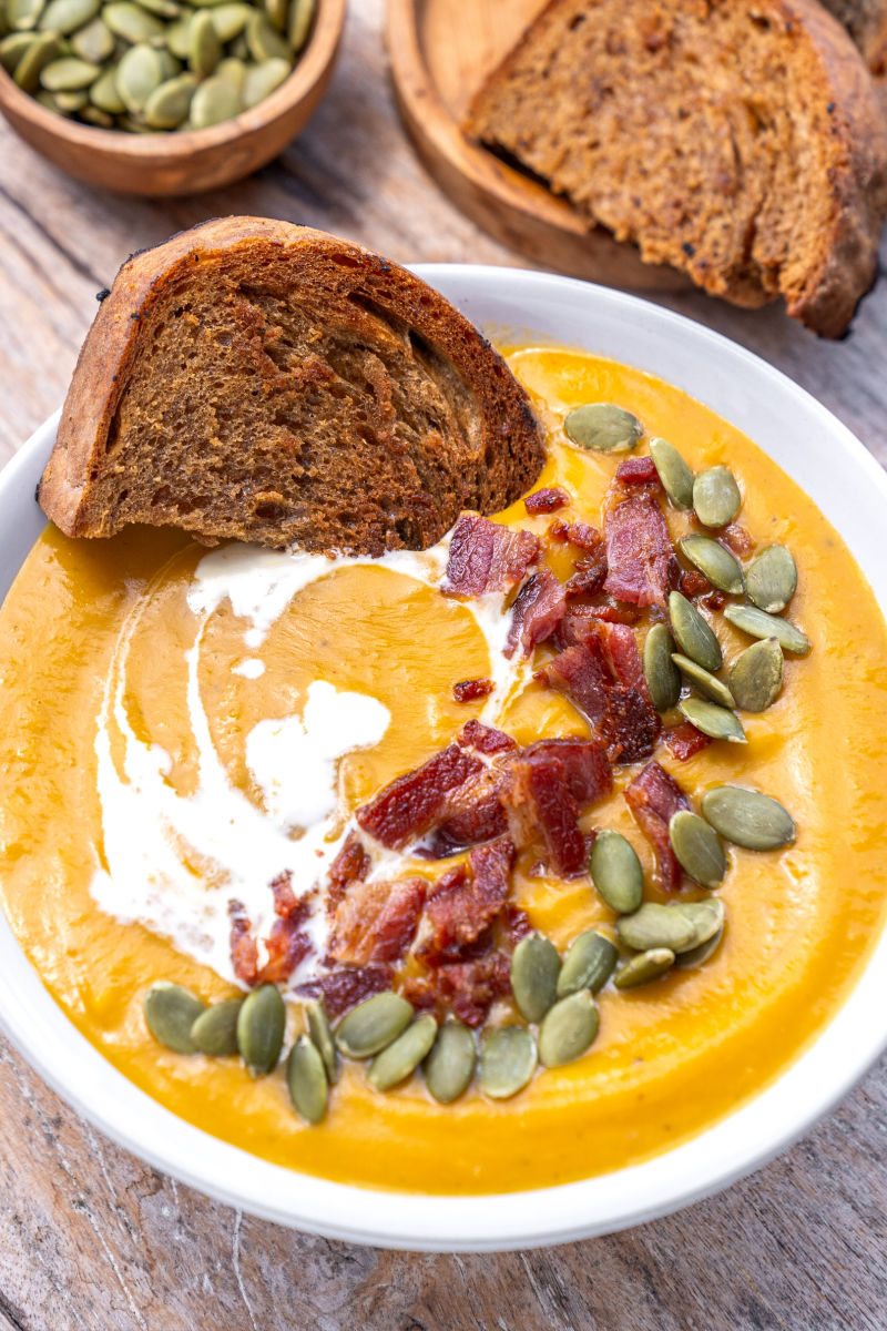 angled view of a bowl of sweet potato soup with a piece of brown bread resting on one side