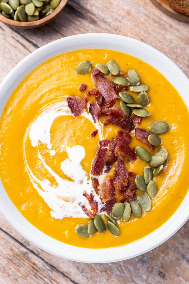 looking down at a bowl of sweet potato soup topped with cream, bacon, and pumpkin seeds
