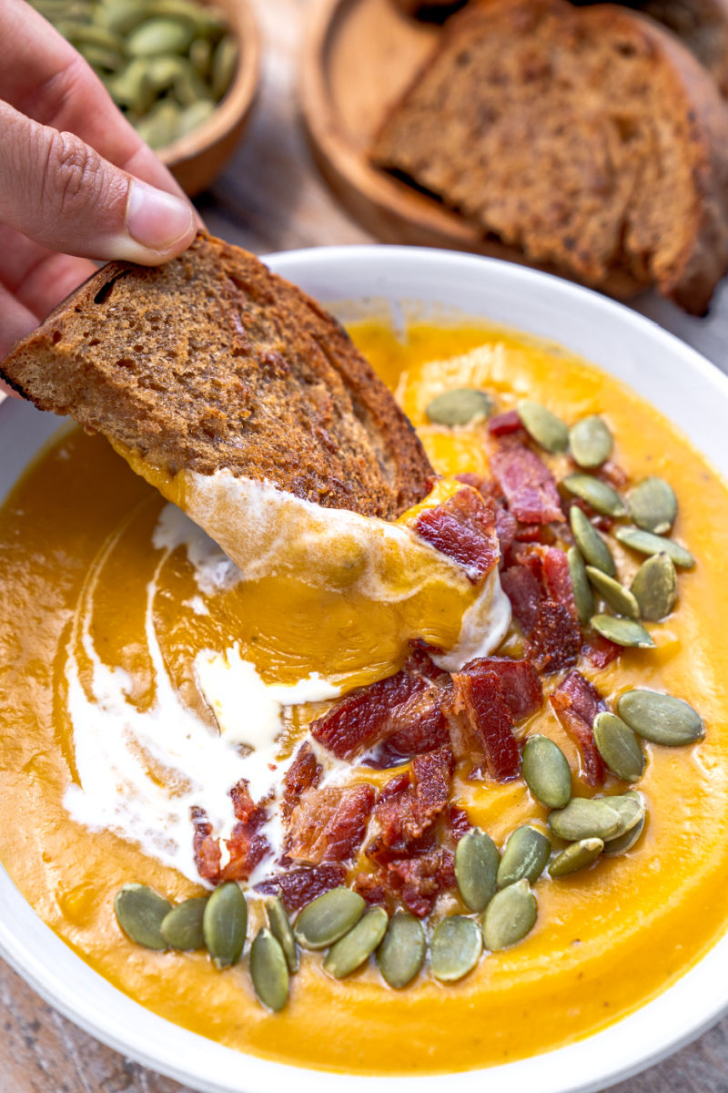 piece of brown bread being dipped into a bowl of sweet potato soup