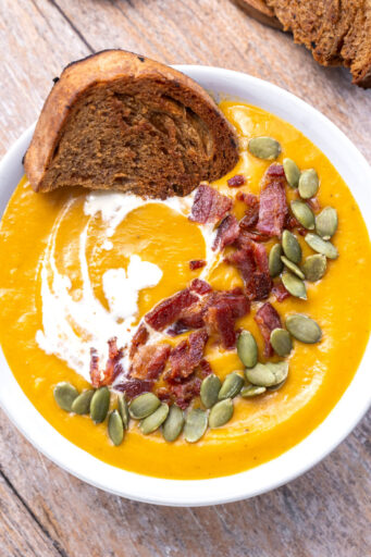 looking down at a bowl of sweet potato soup with a piece of brown bread